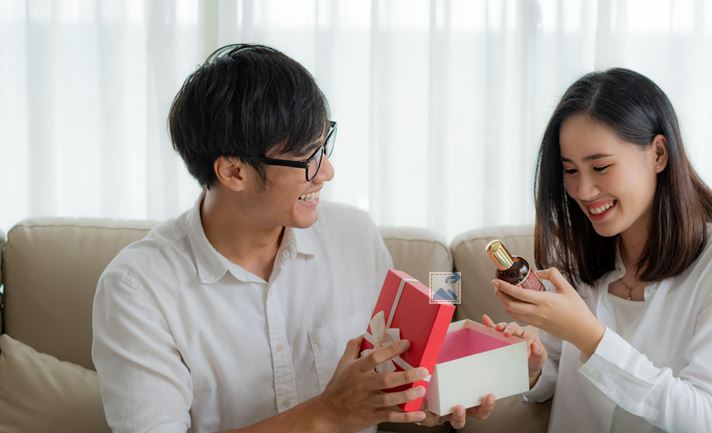 Couple Assis Sur Un Canapé Qui S'offre Une Bouteille De Parfum