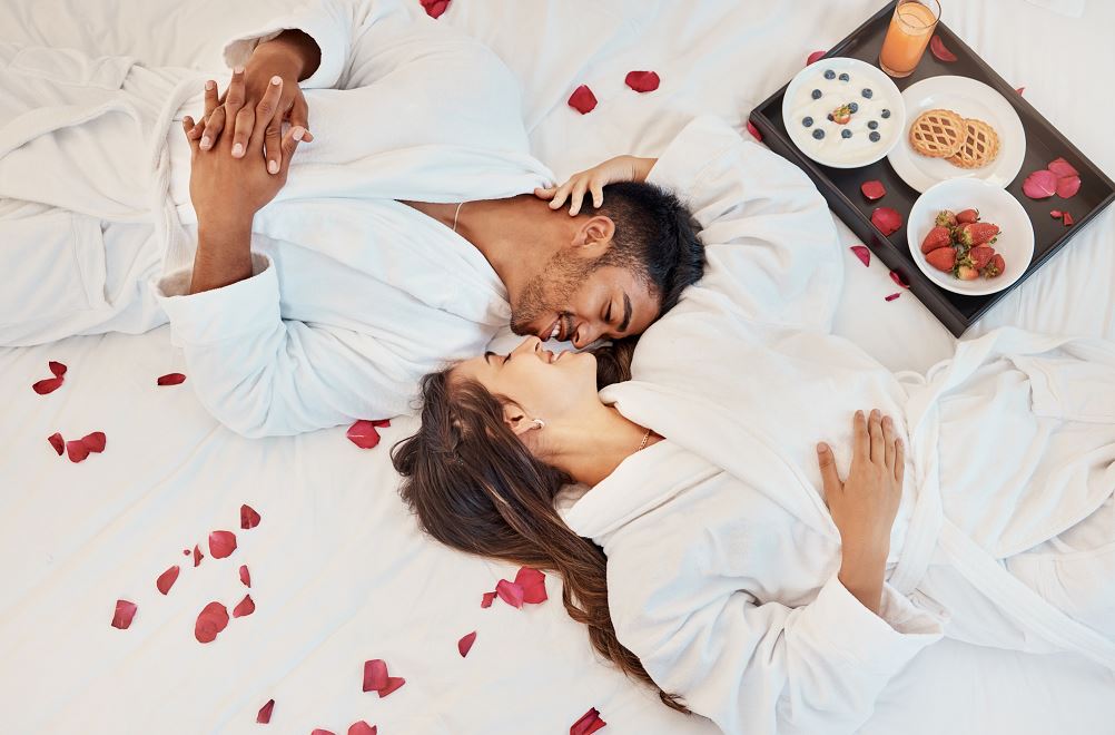 Couple Heureux à L'hôtel, Petit Déjeuner Et Pétales De Rose Au Lit