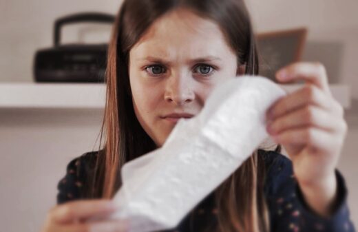 Jeune Fille Tenant Une Serviette Hygiénique Exprimant La Surprise Face à Ses Premières Menstruations